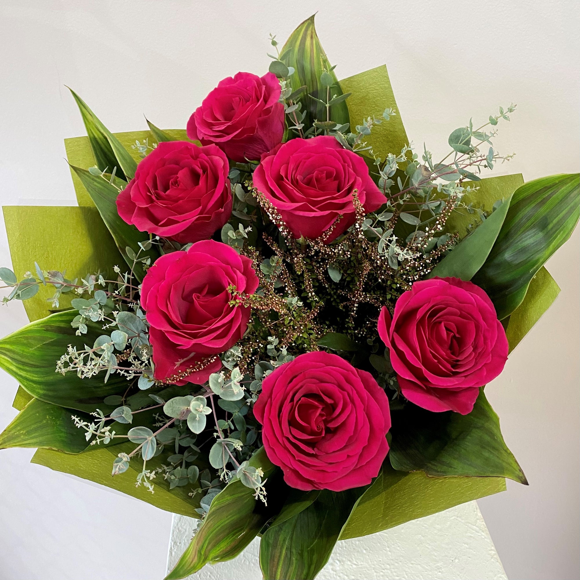 Bouquet of bright pink roses with green leaves on a light background