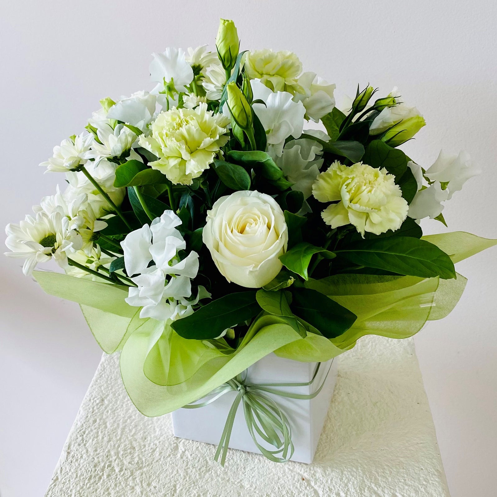 Bouquet of white and light green flowers in a box on a pink background